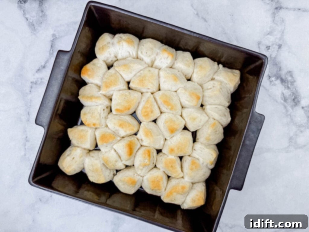 A square baking pan filled with evenly baked, golden-brown pull-apart bread rolls on a marble surface.