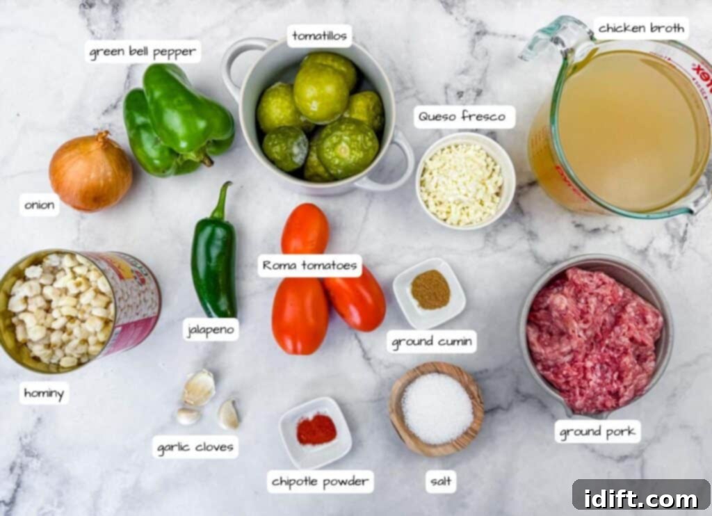 A beautiful flat lay of fresh ingredients for Green Pork Posole Soup on a light marble counter, including ground pork, a can of hominy, green bell pepper, tomatillos, Roma tomatoes, onion, jalapeño, garlic cloves, queso fresco, various spices, and a container of chicken broth.