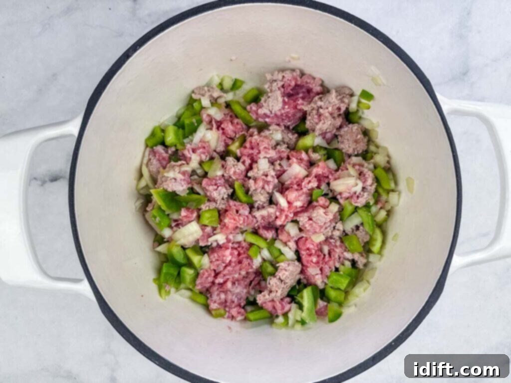 A close-up view inside a white pot on a marble surface, showcasing raw ground pork mixed with finely chopped green bell peppers and diced onions, perfectly prepped and ready for the next cooking stage.