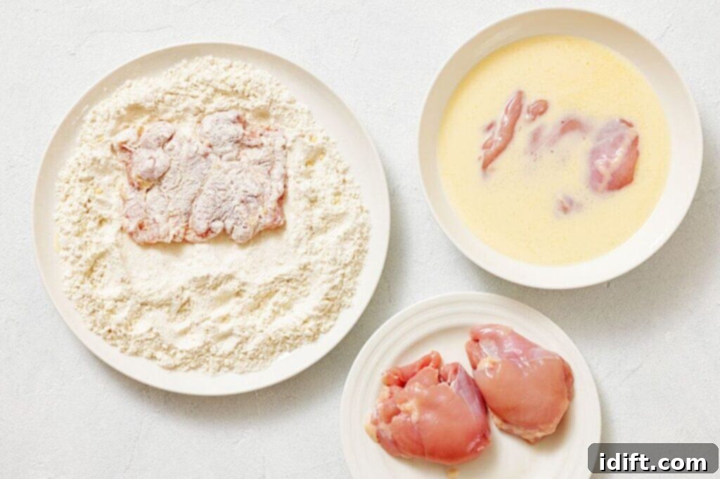 Three plates: one with raw chicken thighs, one with raw chicken in egg wash, and one with chicken pieces coated in flour.