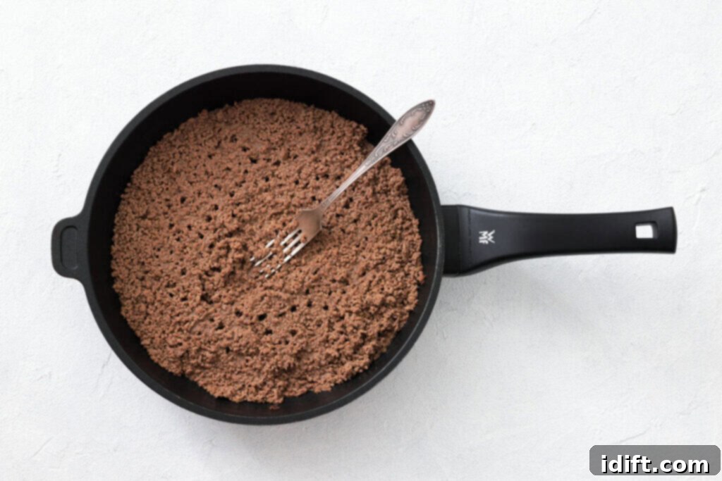 The Queen City's Signature Bowl 5 A pan filled with cooked ground beef sits on a light surface; a metal fork rests inside the pan.