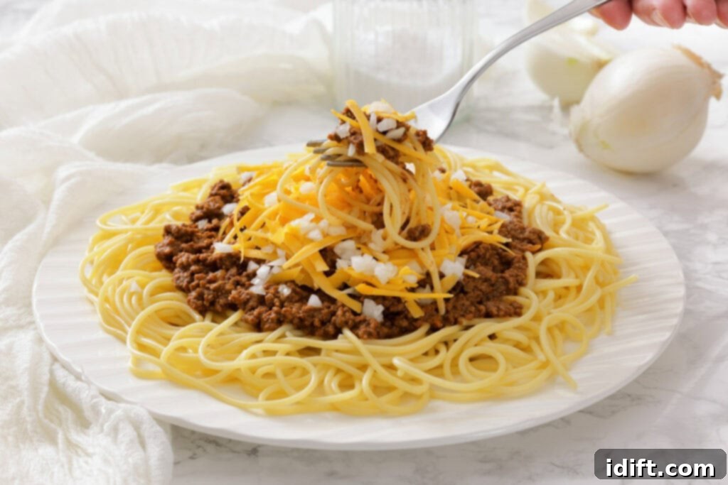 The Queen City's Signature Bowl 8 A plate of spaghetti topped with chili, shredded cheddar cheese, and chopped onions, with a fork lifting a portion.