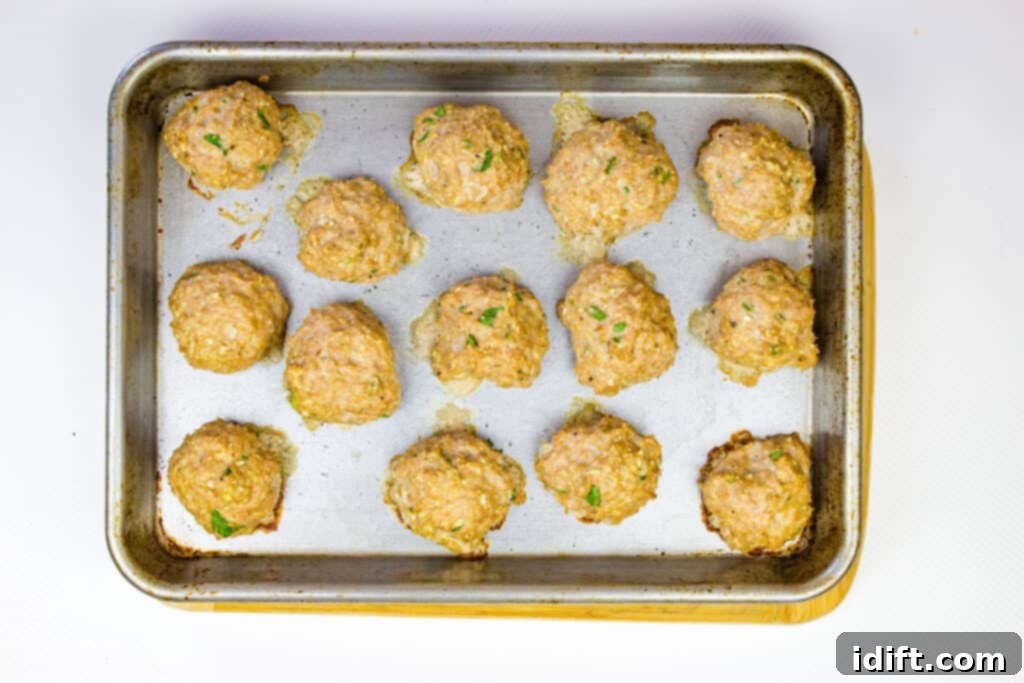 Savory Marsala Chicken Meatballs 9 Cooked meatballs arranged on a parchment-lined sheet tray after baking.