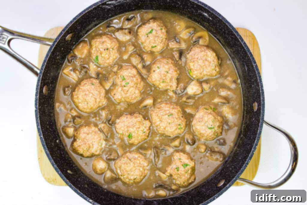 Savory Marsala Chicken Meatballs 13 The Marsala sauce simmering in a skillet, with cooked meatballs added in, being gently coated.