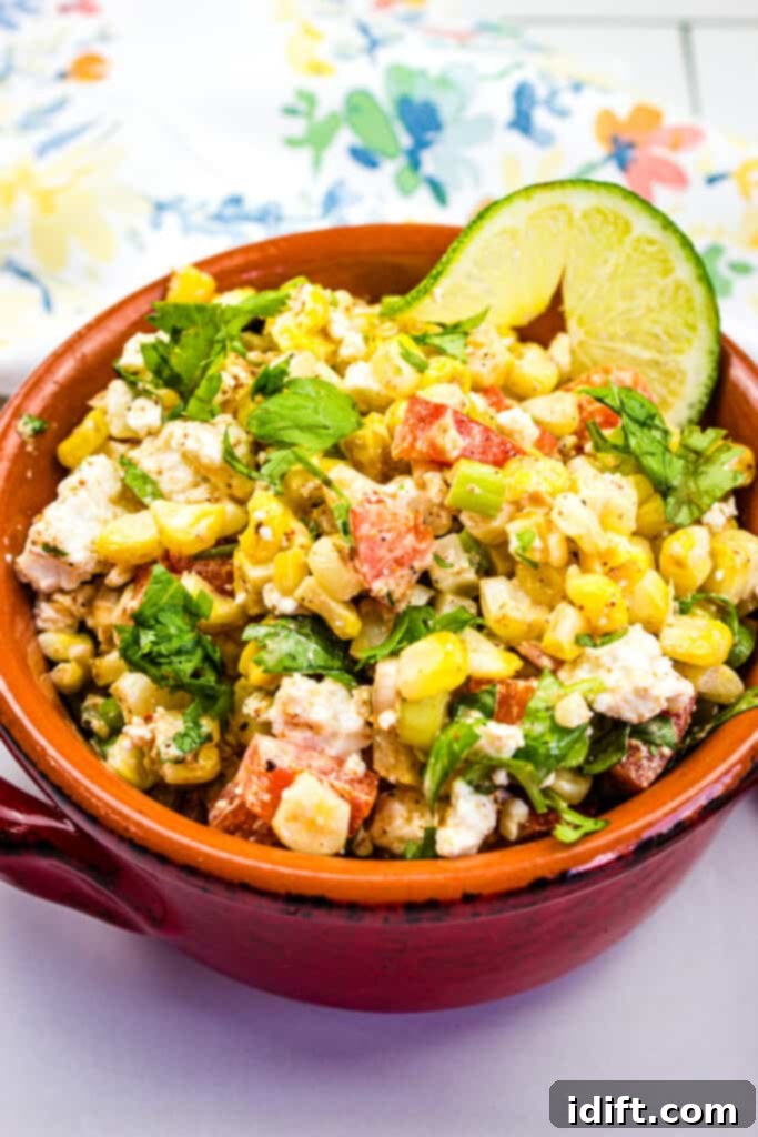 Vibrant Mexican Street Corn Salad in a rustic bowl, garnished with fresh cilantro and a lime wedge.