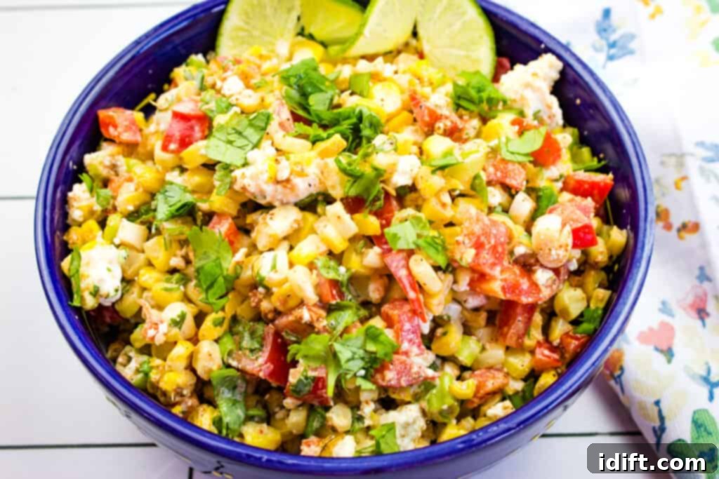 A vibrant close-up of Mexican street corn salad in a blue serving bowl, garnished with a lime wedge and cilantro.