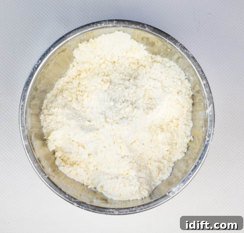 A pastry blender cutting cold butter into the flour mixture, creating coarse crumbs for the biscuit dough.