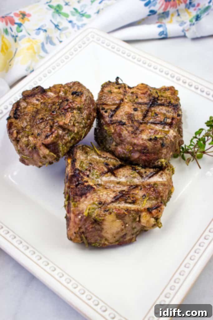 Two perfectly smoked lamb chops on a white plate with a sprig of rosemary