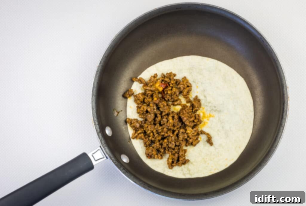 Beef and cheese filling being spooned onto half of a tortilla