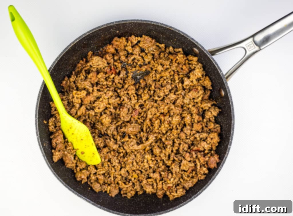 Ground beef browning in a skillet with spices being added