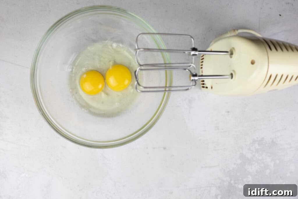 Tangy Cranberry Squares 13 Eggs being vigorously whipped in a bowl using an electric mixer until they are light and frothy.