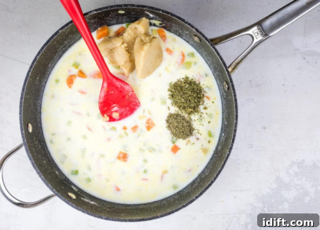 Hot milk, gravy, herbs, salt, and pepper being added to the thickened vegetable mixture.
