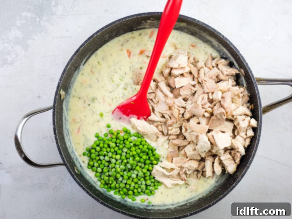 Cooked turkey chunks and frozen peas being added to the creamy pot pie filling.
