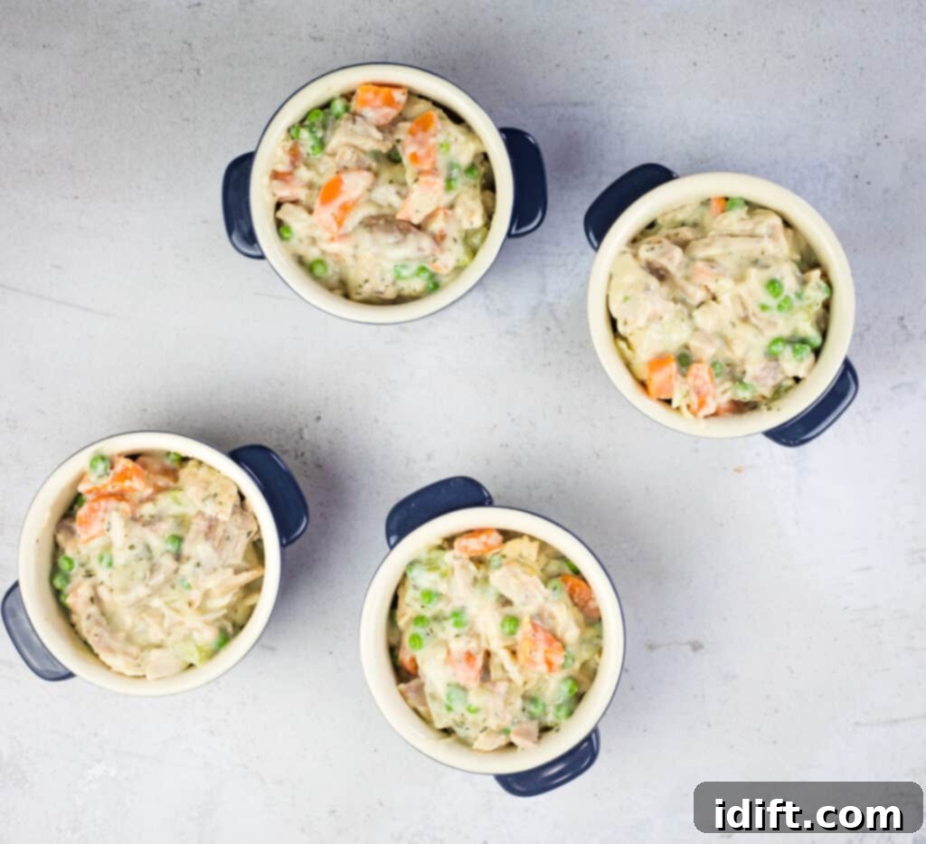 The creamy turkey pot pie filling being spooned into individual ramekins.