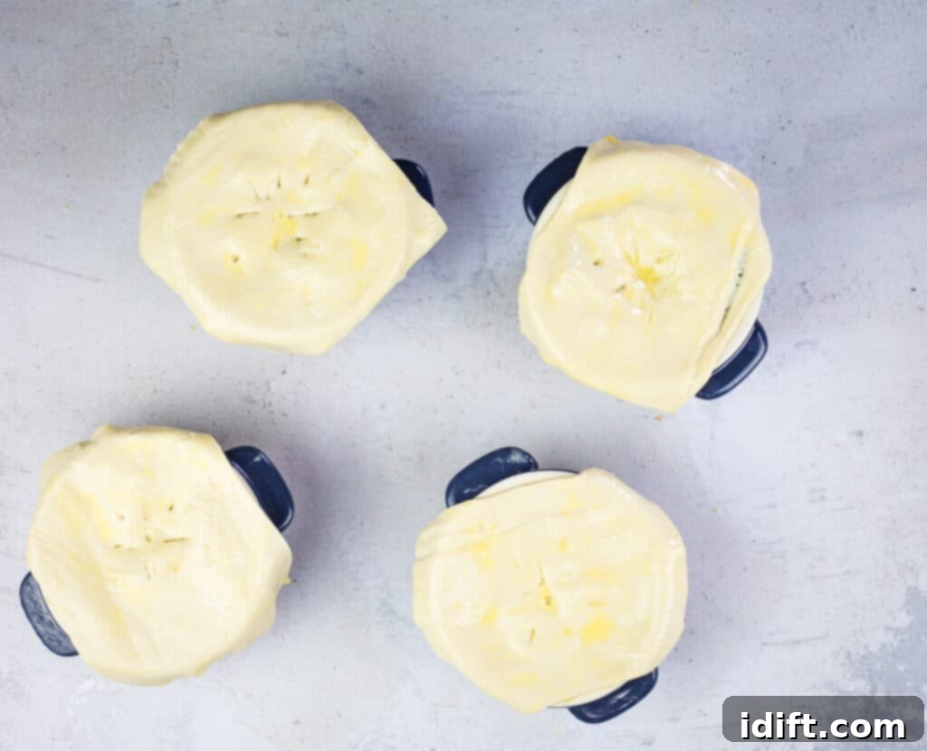Turkey pot pie with puff pastry in small dishes being brushed with egg wash.