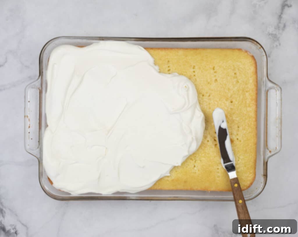 Applying whipped cream icing to the top of the chilled Eggnog Tres Leches cake.