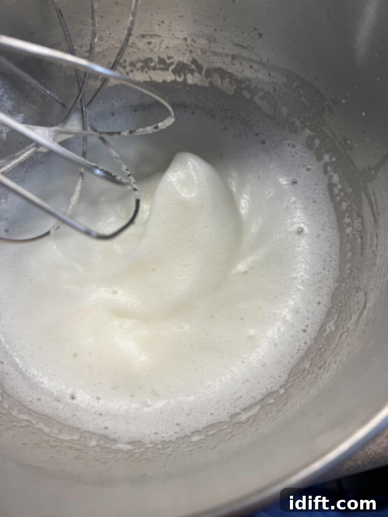 A mixer bowl filled with fluffy, whipped egg whites and sugar.