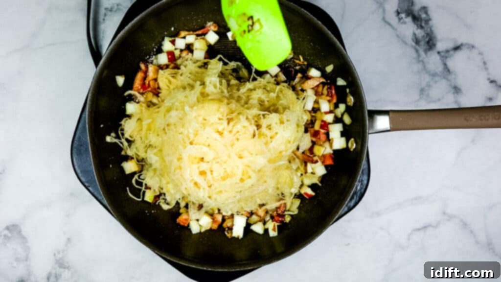 Mixing drained sauerkraut into the sautéed mixture of bacon, onions, and apples.