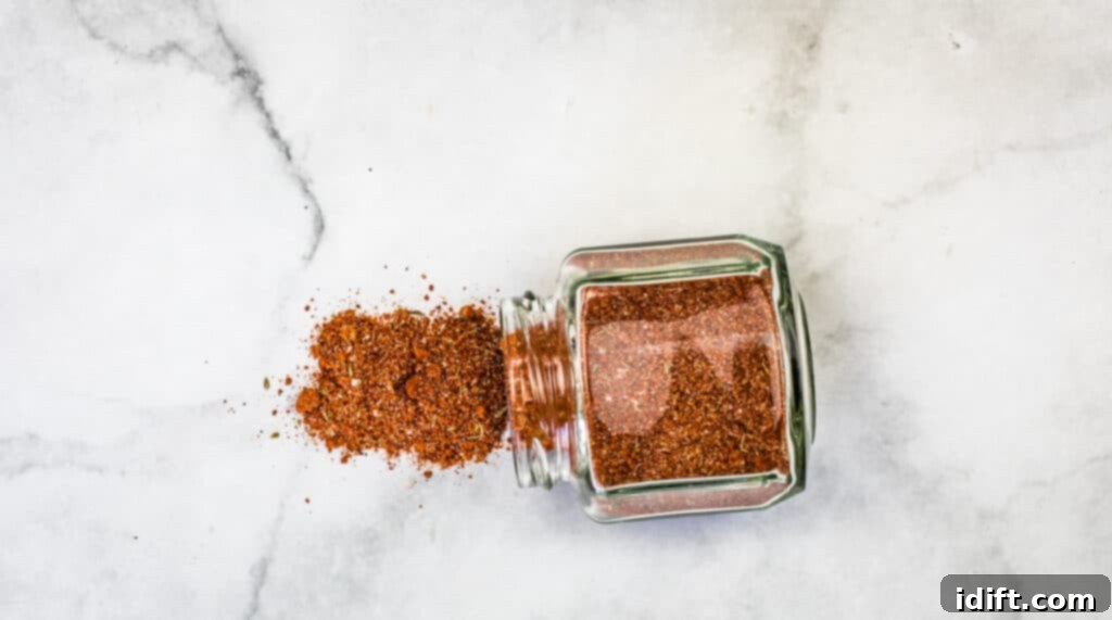 The Best Pork Rub spilling out of a glass jar, showcasing its rich texture