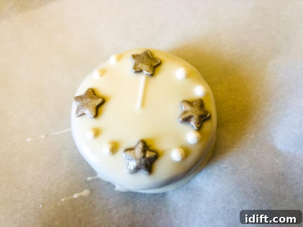 A freshly dipped cookie, still damp with white chocolate, being topped with an assortment of vibrant sprinkles to represent the hours and minutes of a clock.