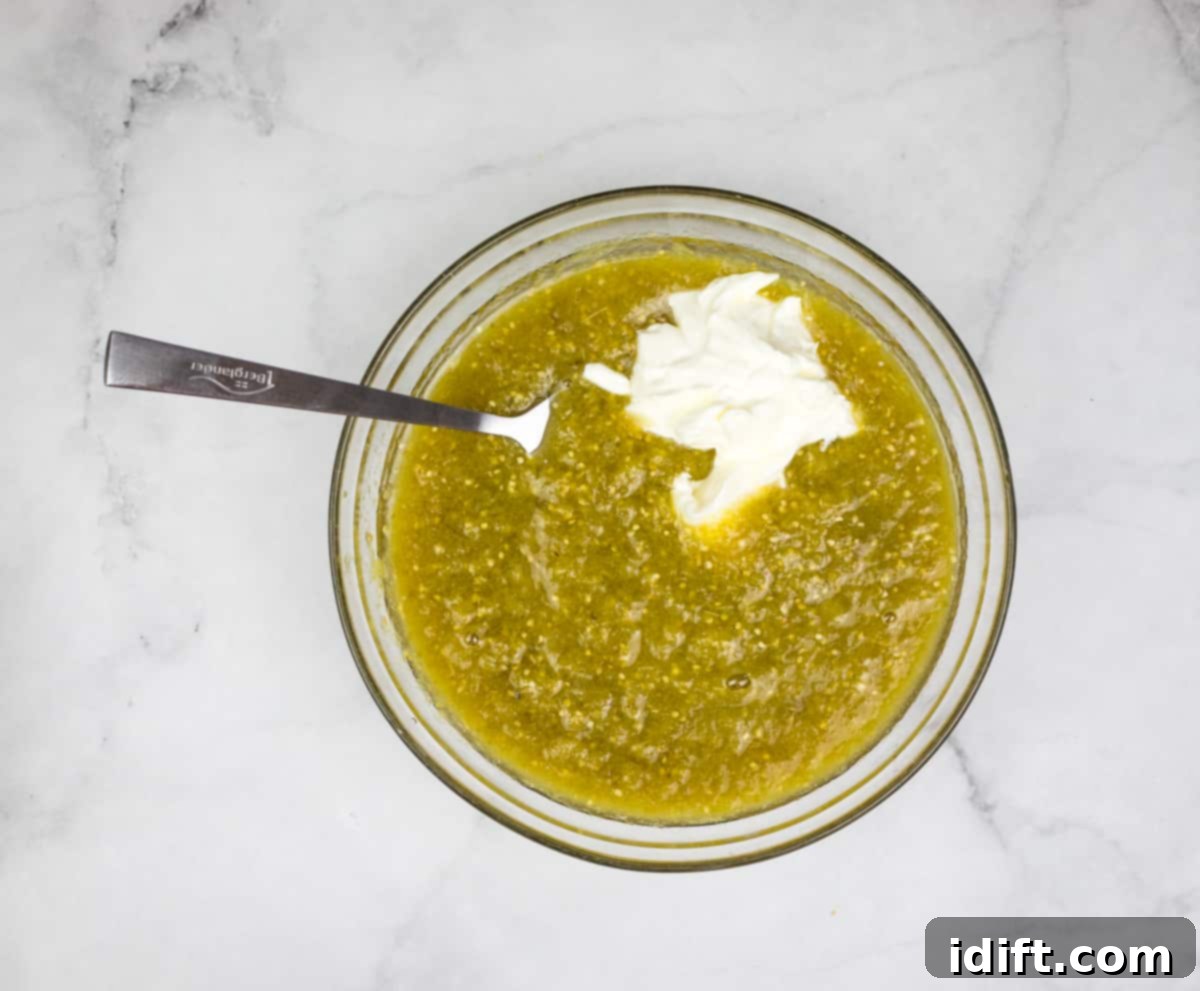 Mixing sour cream into a bowl of sauce for smoked chicken enchiladas.