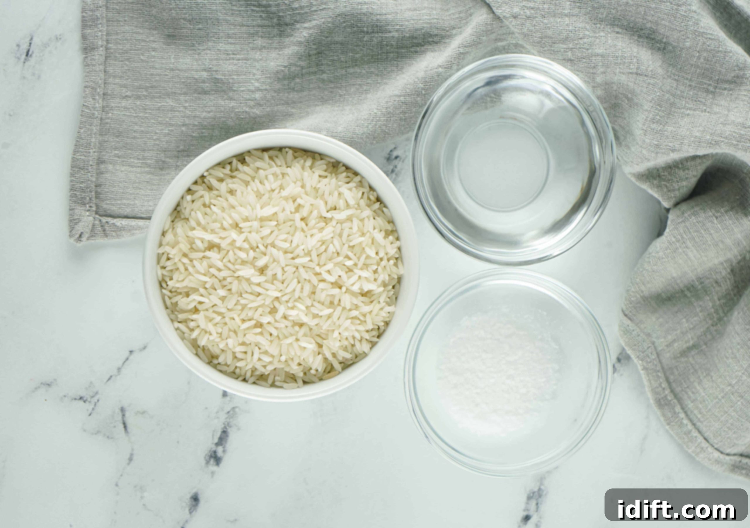 Foolproof Instant Pot Rice 4 Ingredients laid out for cooking rice in an Instant Pot: a bowl of white rice, a container of water, and a salt shaker.
