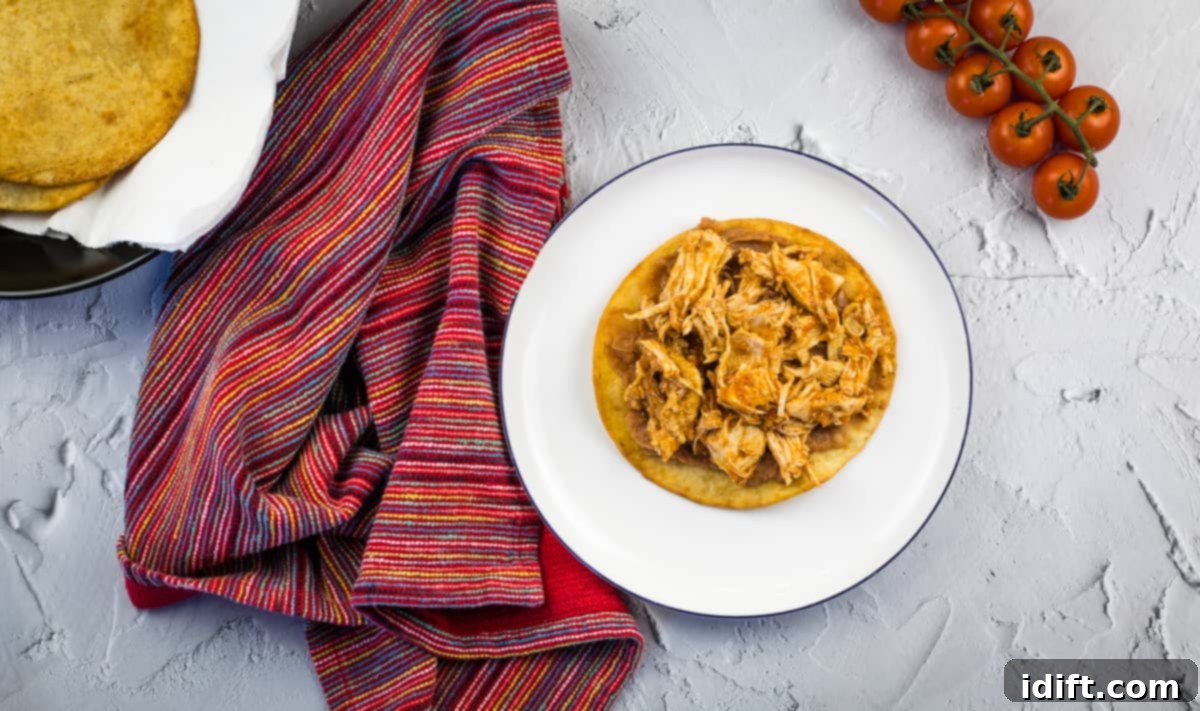 A tostada base spread with refried beans and a generous topping of chicken tinga, ready for more garnishes.