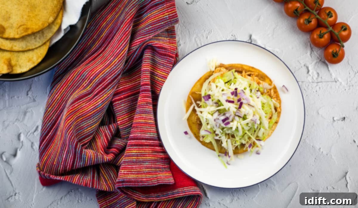A fully loaded chicken tinga tostada on a plate, adorned with shredded lettuce, cheese, onions, and other fresh toppings.