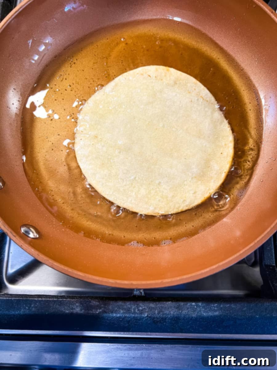 A corn tortilla sizzling and turning golden brown as it fries in hot oil within a skillet.
