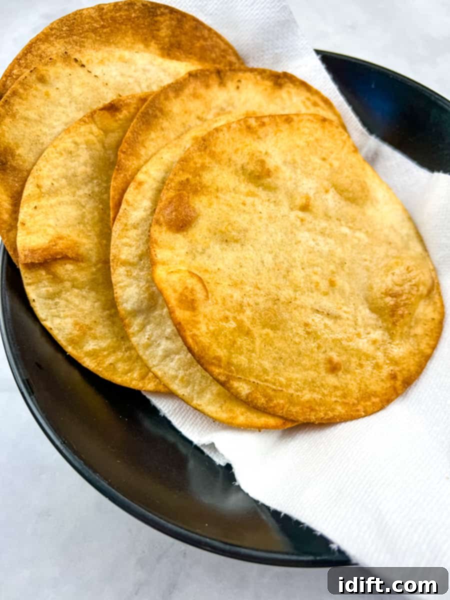 A stack of freshly fried, homemade tostadas draining on paper towels to remove excess oil.