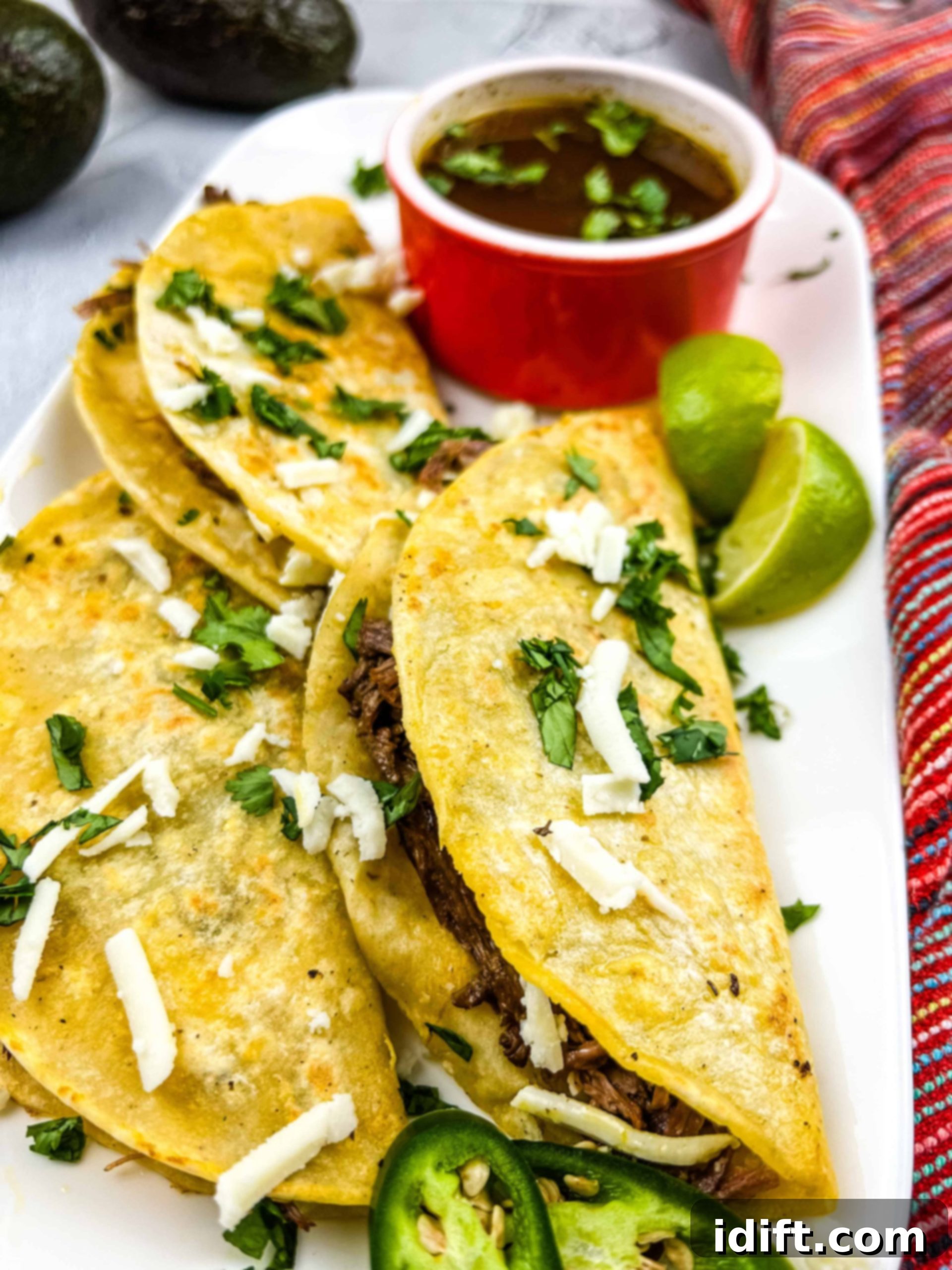 birria tacos on a plate with a cup of jus in the background