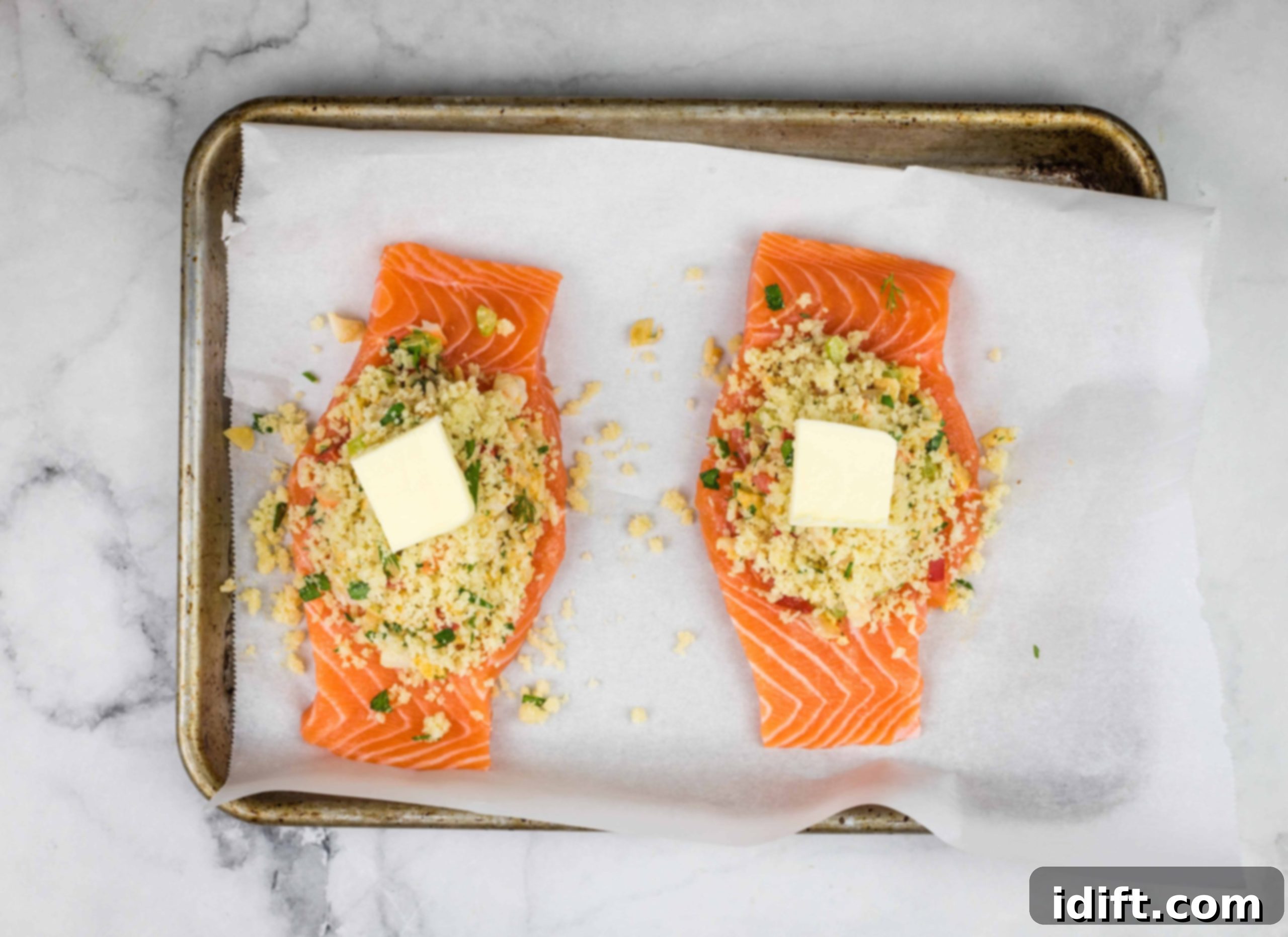 Salmon fillets on a baking sheet, topped with small knobs of butter.