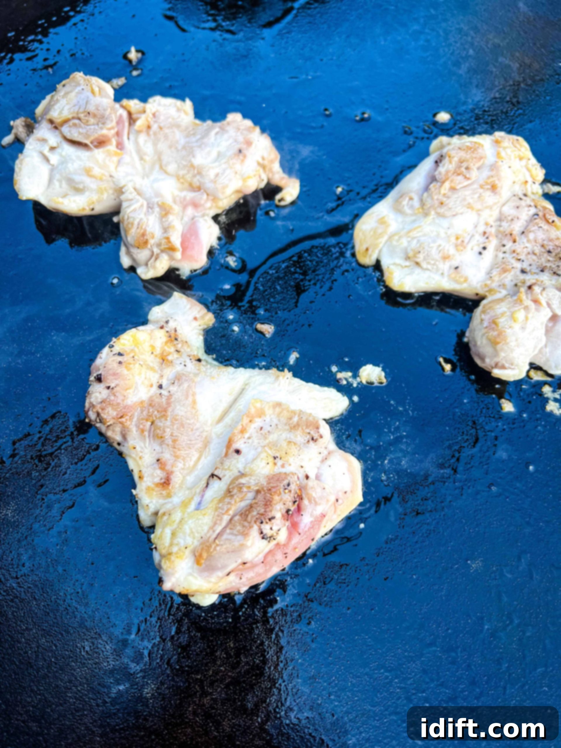 Cooking seasoned chicken thighs on a hot Blackstone griddle until perfectly seared.