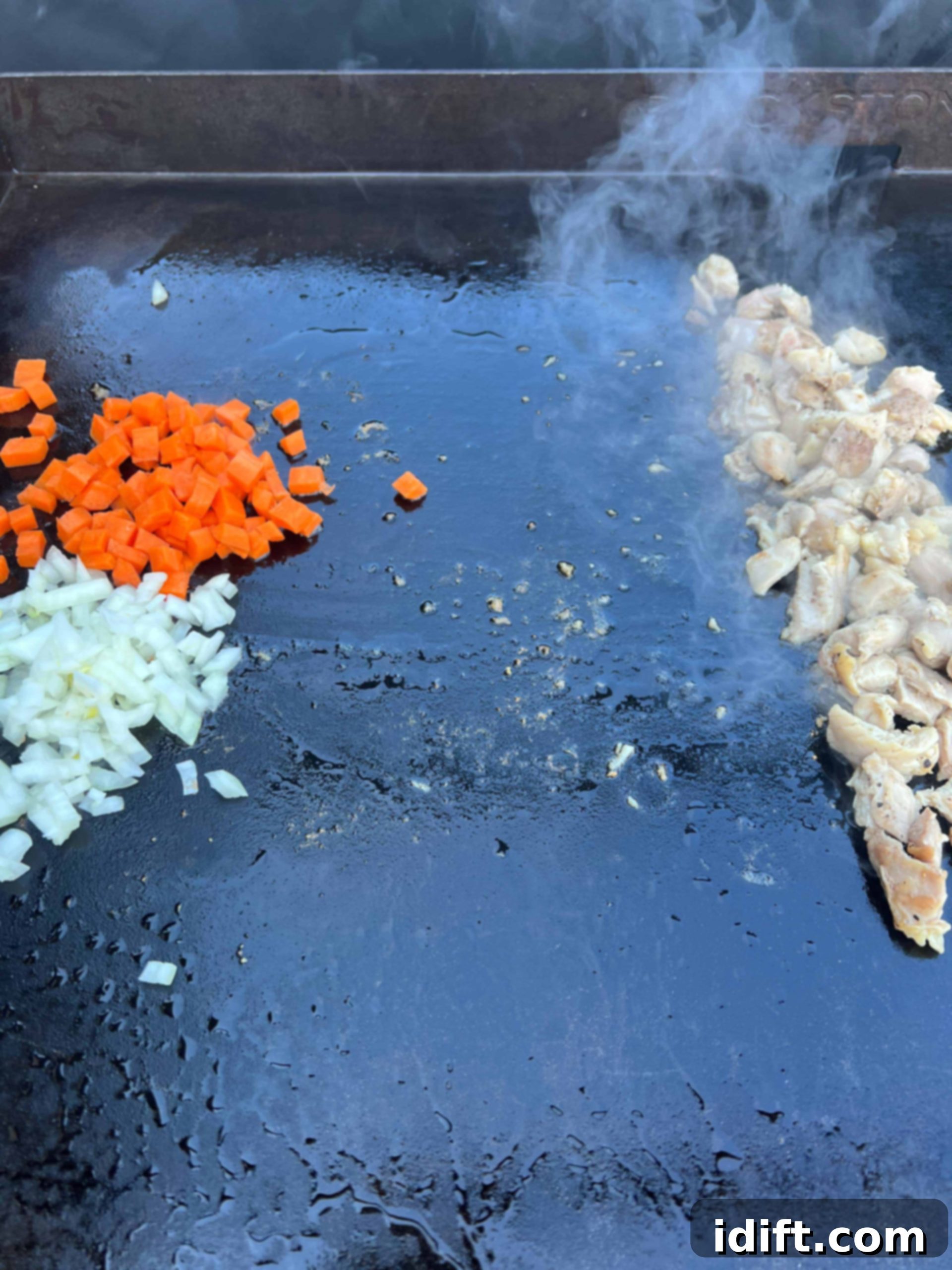 Sautéing onions and carrots on the griddle while chopped chicken finishes cooking to the side.