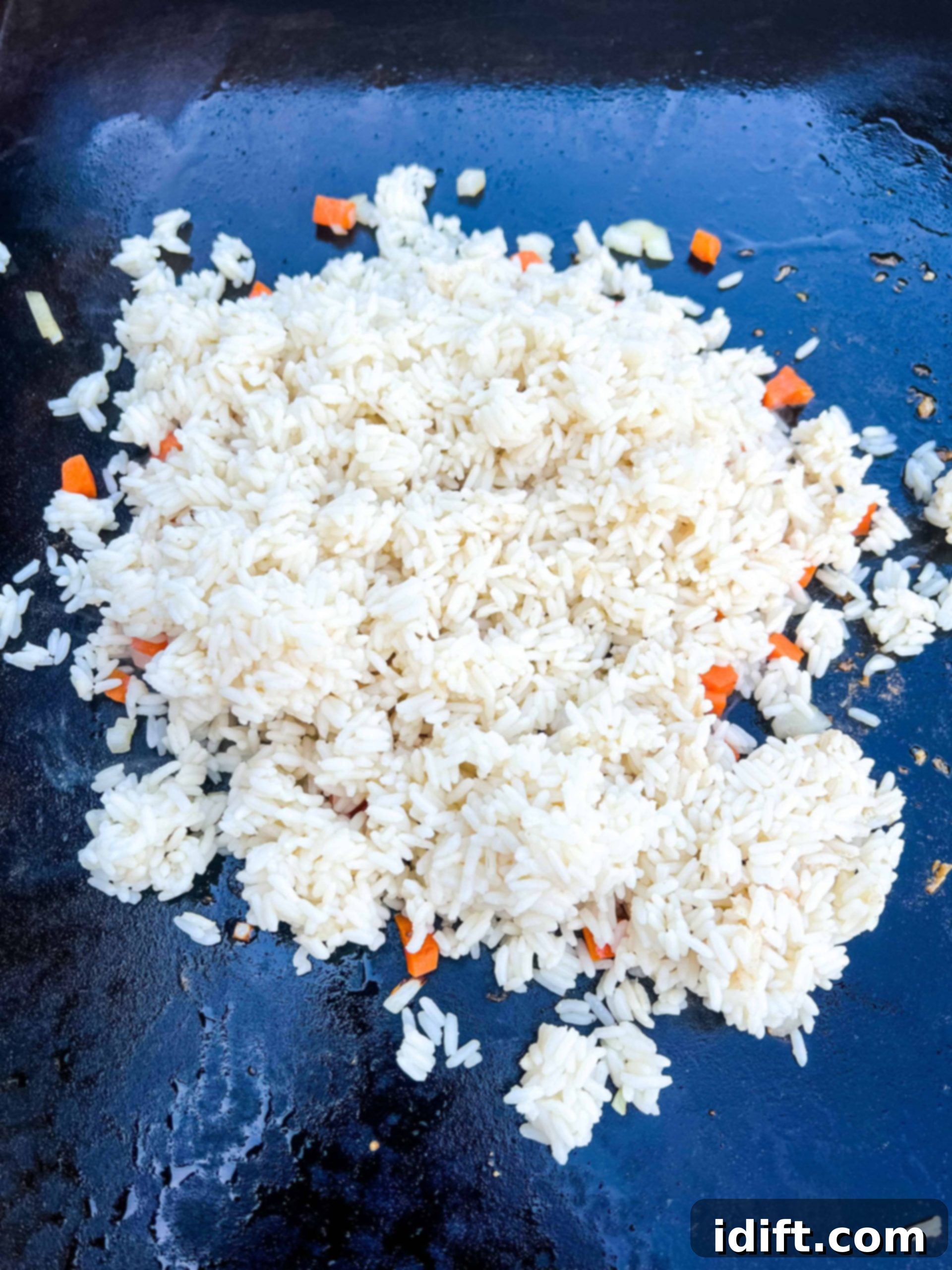 Adding day-old rice to the griddle with the vegetables, ready for frying.