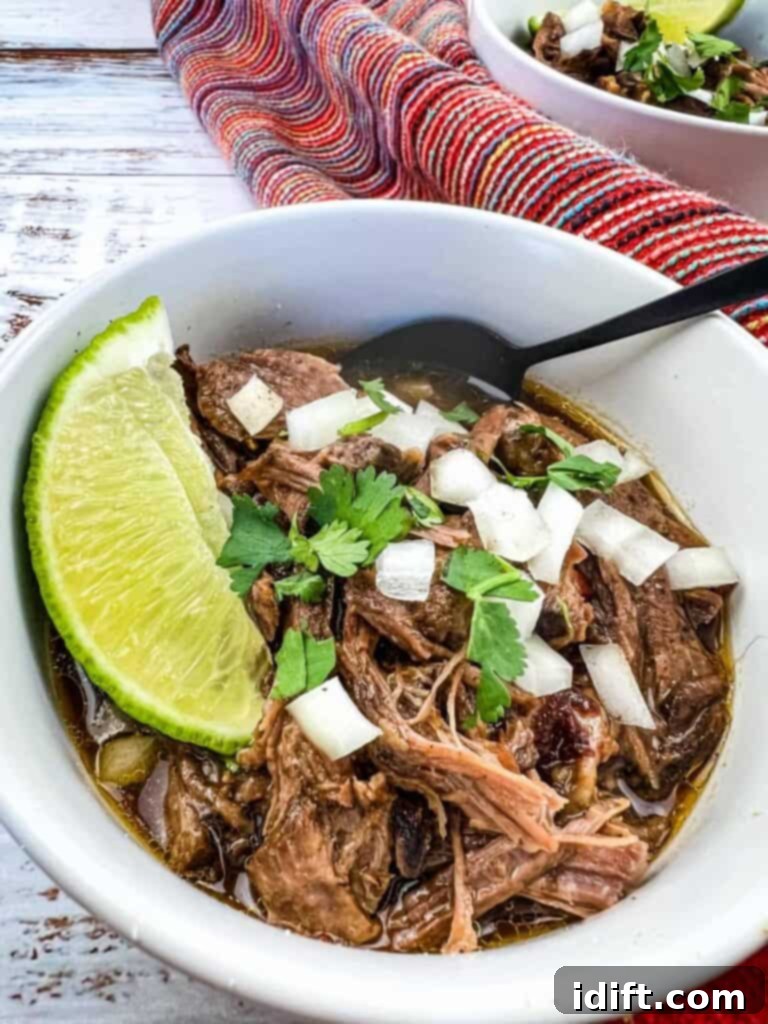 Tender Slow Cooker Birria de Res 2 A bowl of Mexican beef stew with lime wedges, ready to be served.