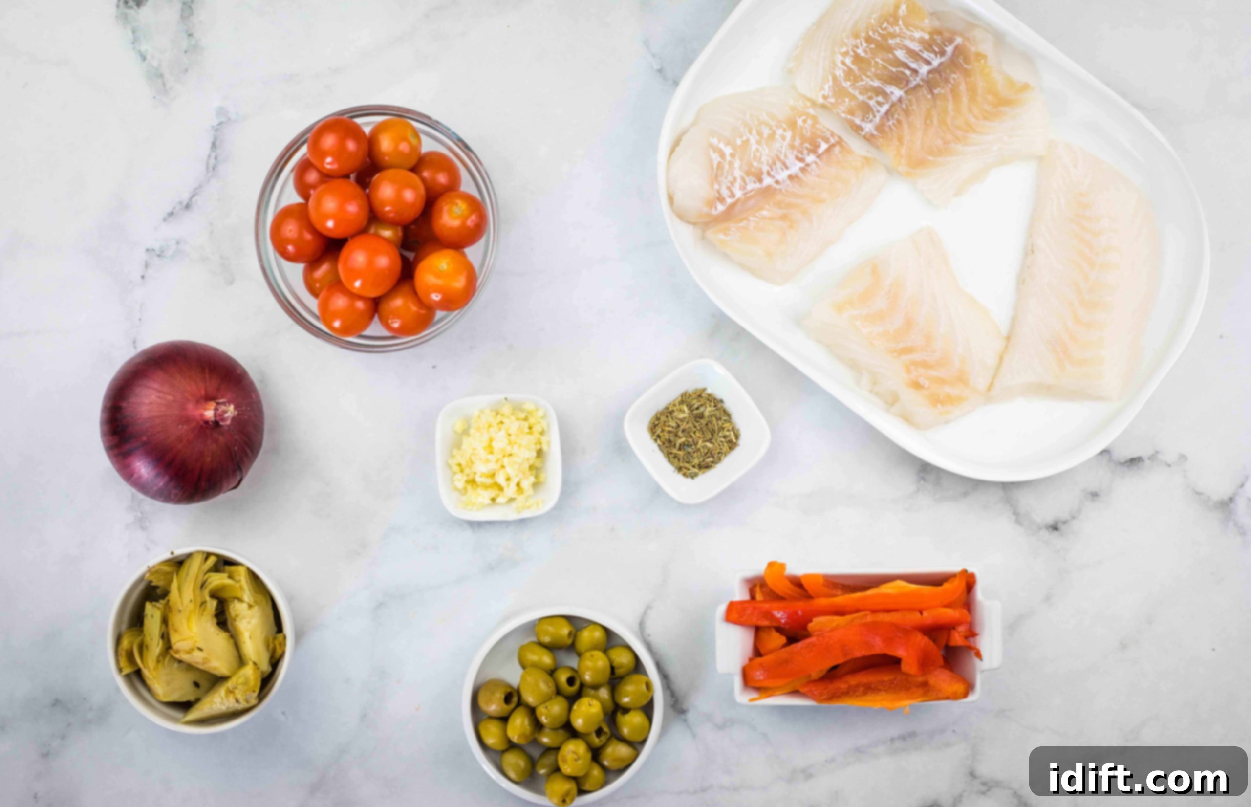 Various fresh ingredients for Mediterranean cod, including cod fillets, cherry tomatoes, red onion, garlic, bell pepper, artichoke hearts, olives, olive oil, and herbs.
