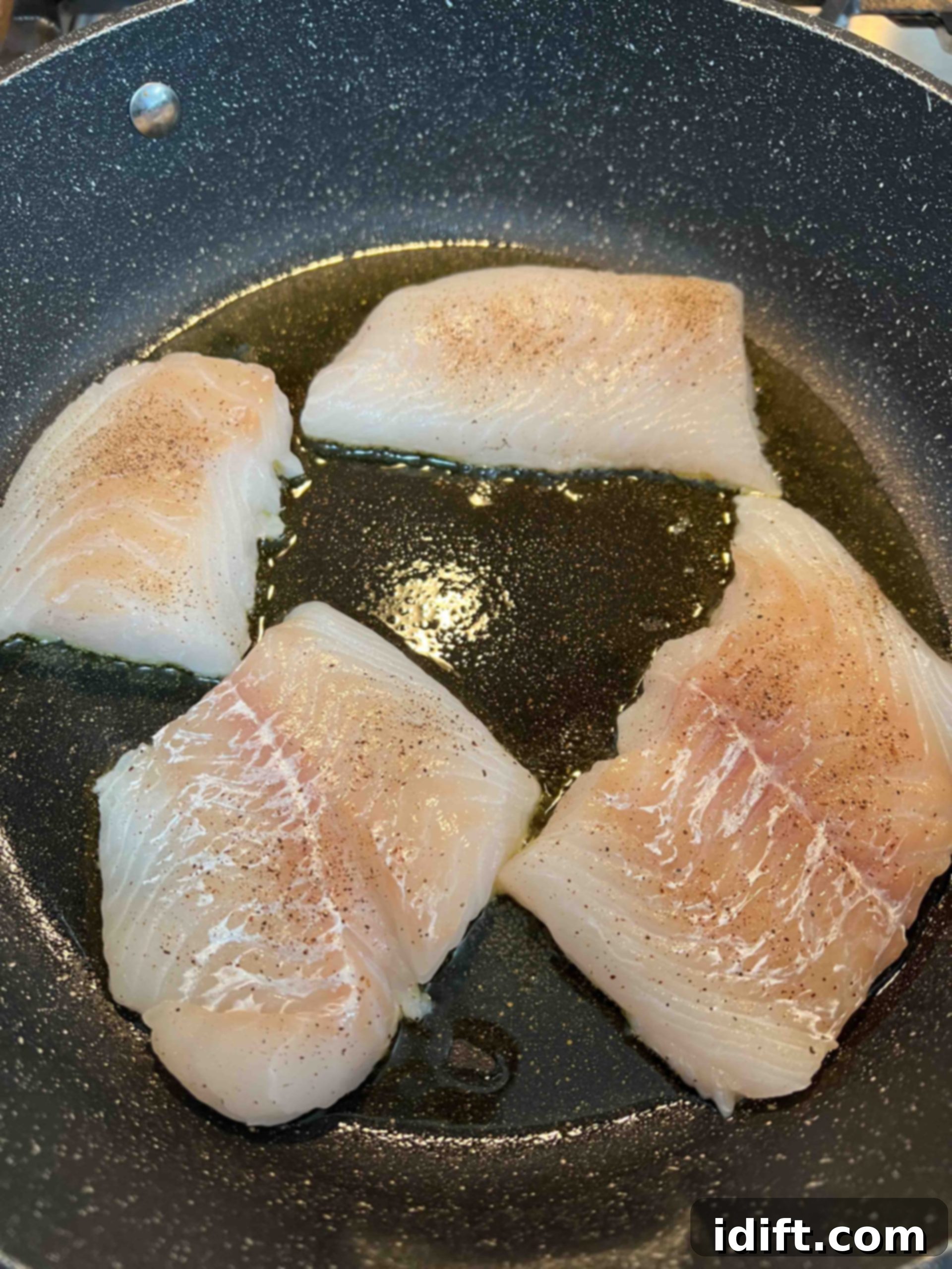 Seasoned cod fillets being pan-fried in olive oil in a skillet, turning golden brown.