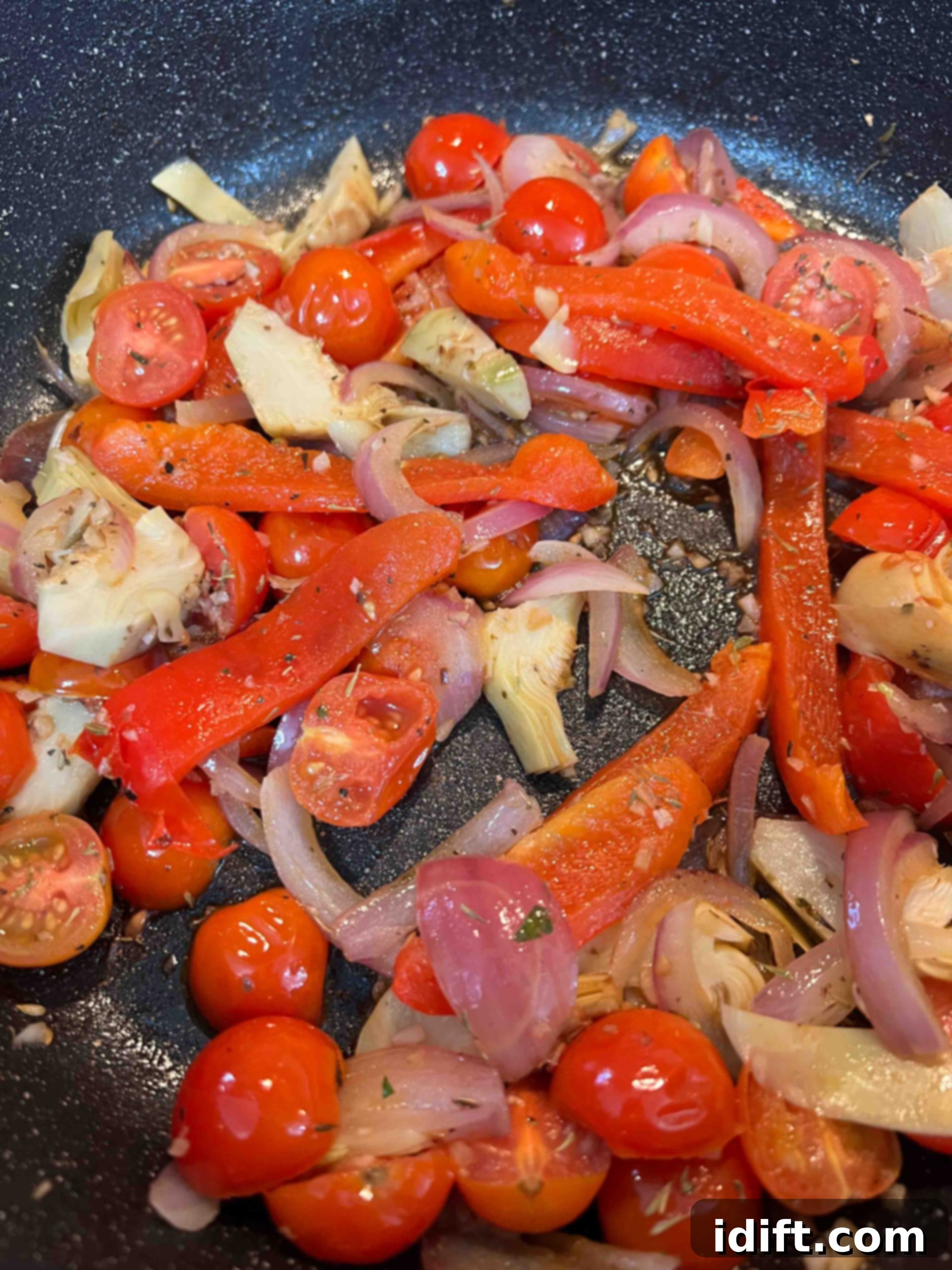 Red onions, garlic, red bell pepper, and cherry tomatoes sautéing in a skillet, softening and blistering.