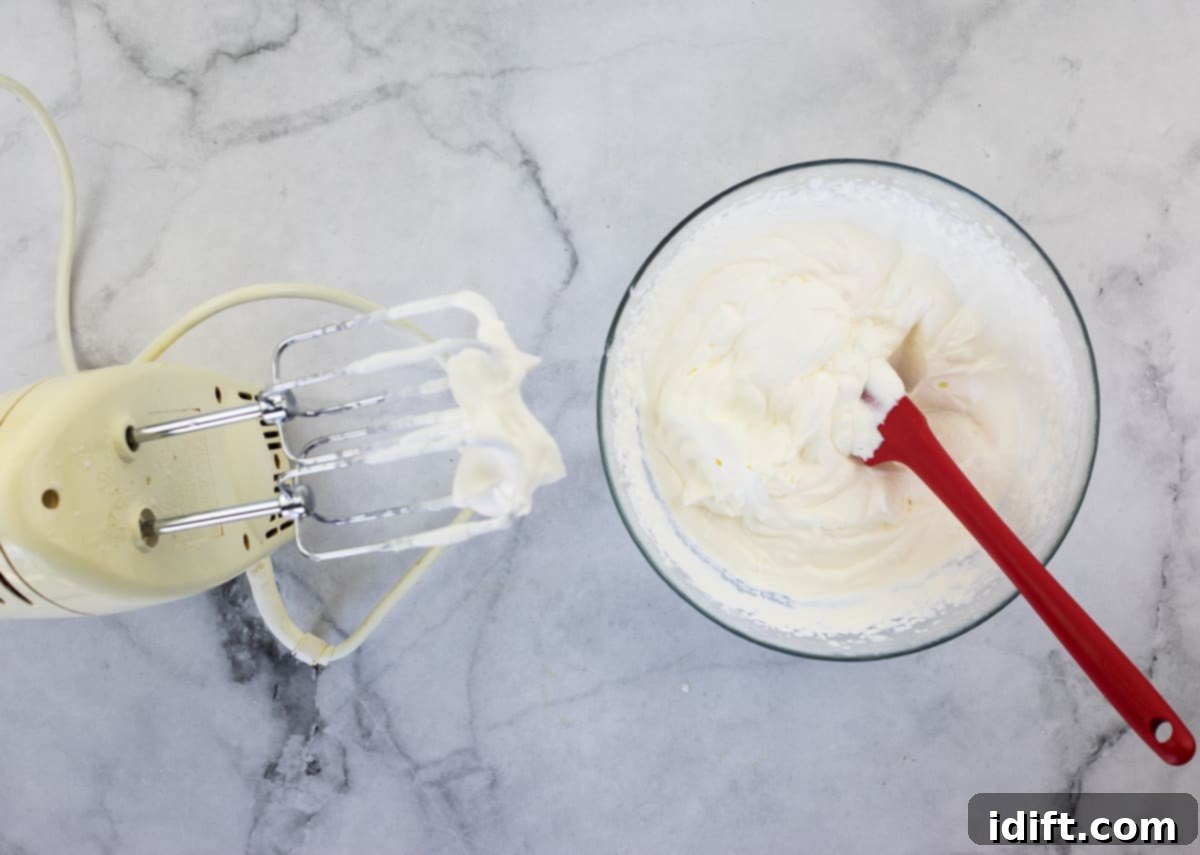 Heavy cream whipped into stiff peaks in a bowl, with dissolved gelatin liquid being drizzled in.