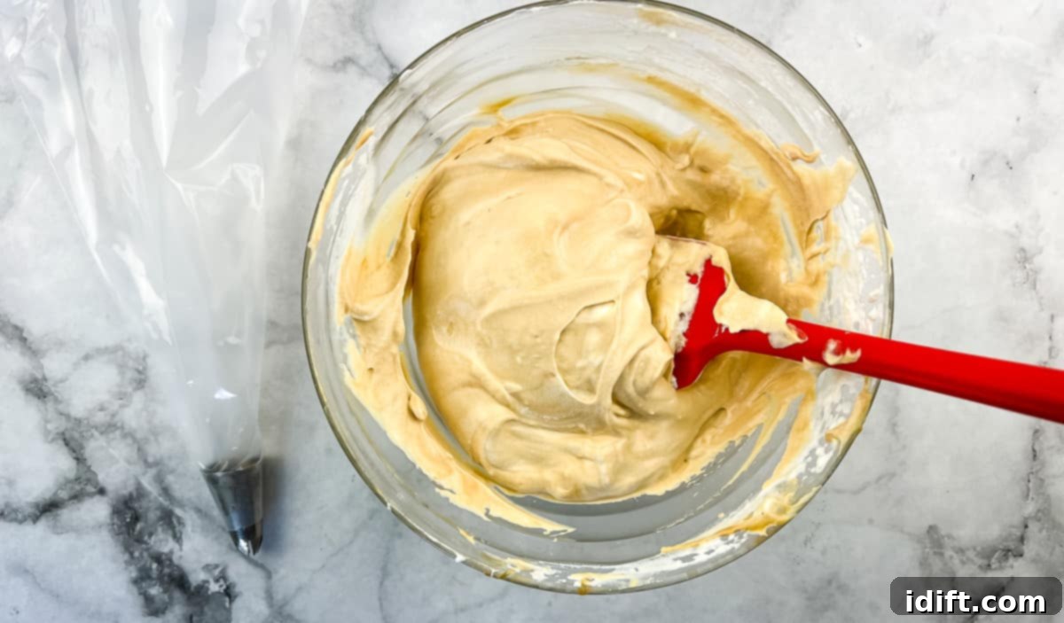 Dulce de leche being folded into the whipped cream and gelatin mixture with a spatula in a large mixing bowl.