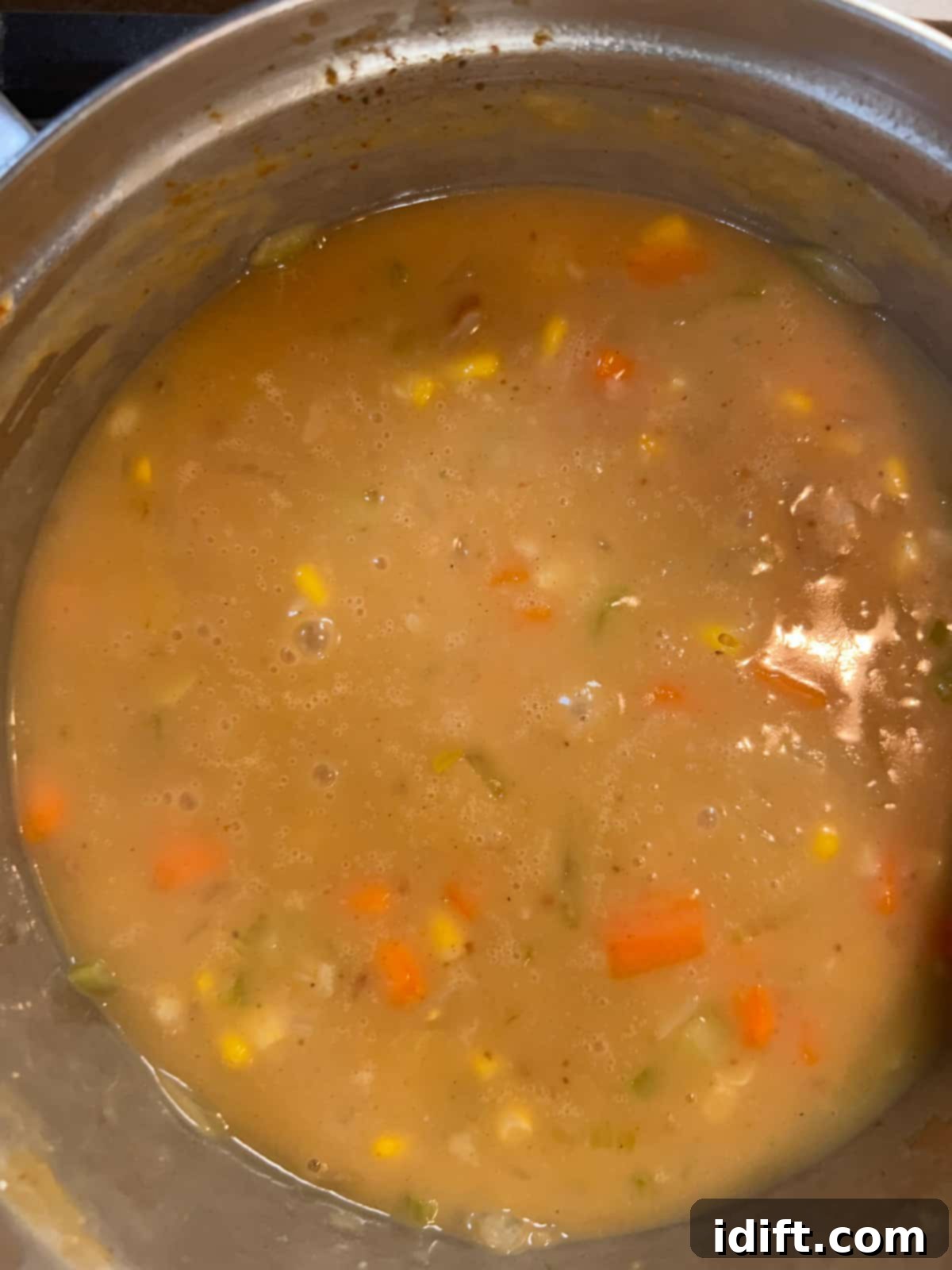 Lobster stock being whisked into the vegetables and roux, forming the liquid base of the chowder, which then simmers to develop flavor.