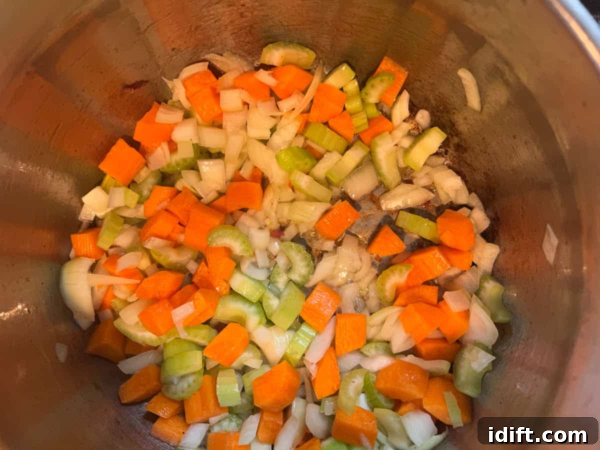 Diced onions, carrots, and celery sautéing in bacon fat and butter in a soup pot, softening to release their aromatic flavors.