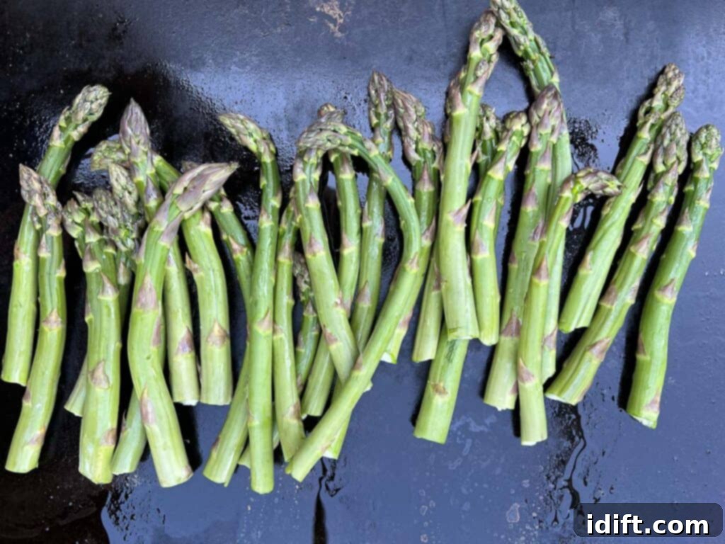 Perfectly Seared Blackstone Asparagus 3 Fresh asparagus spears cooking on a large, hot flat top griddle, showing the vibrant green color and initial char.