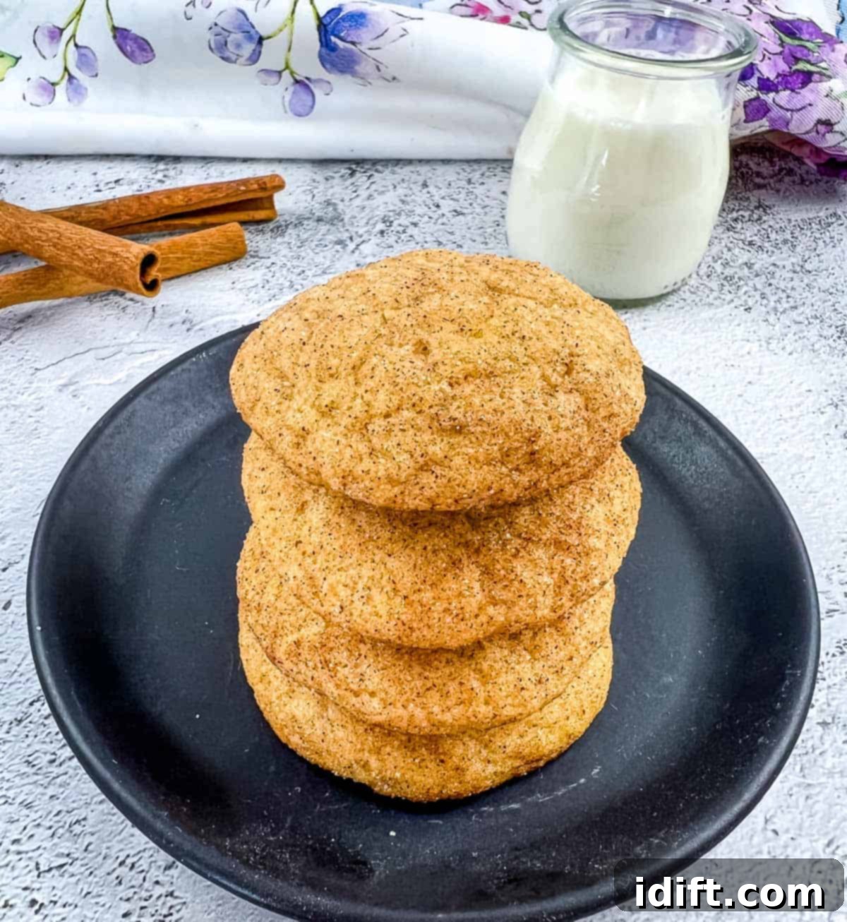Stacked pumpkin snickerdoodles on a plate next to a glass of milk, evoking cozy autumn vibes.