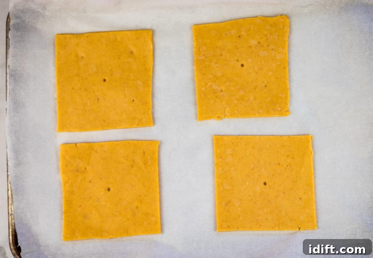 Cheez-It squares neatly arranged on a parchment-lined baking sheet, ready for the oven.