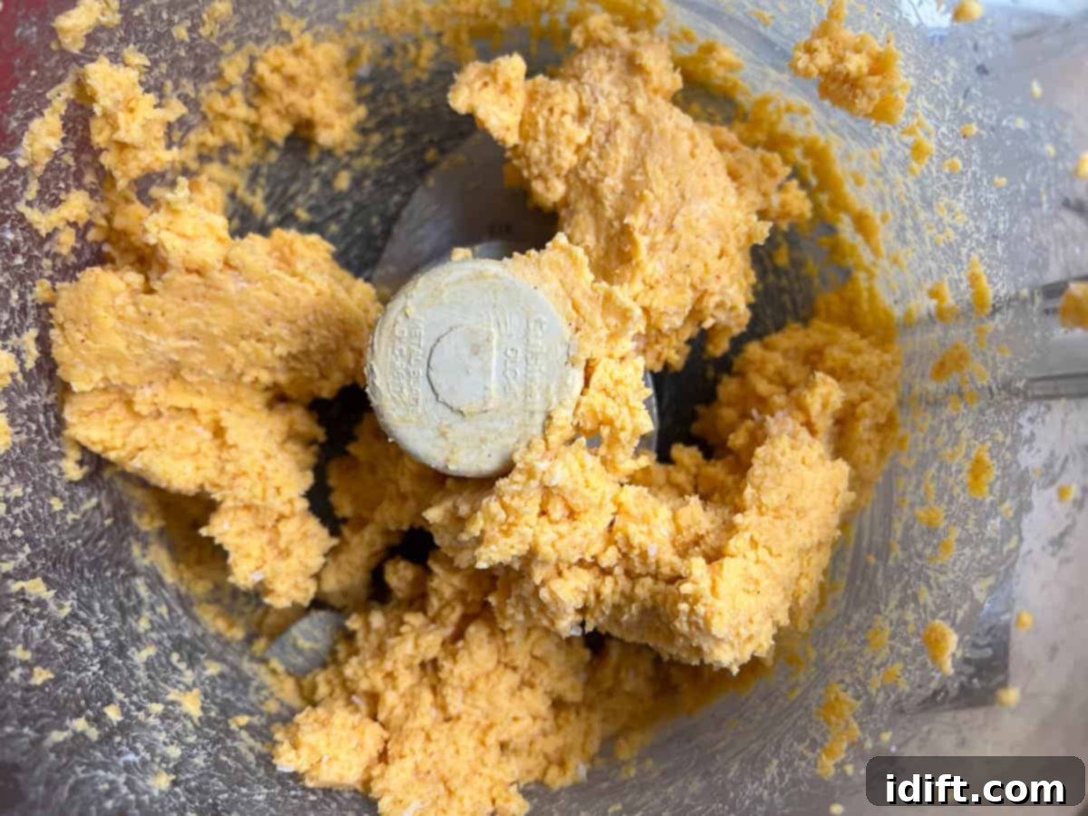 Cheddar cheese and butter being mixed in a food processor, creating a creamy base.
