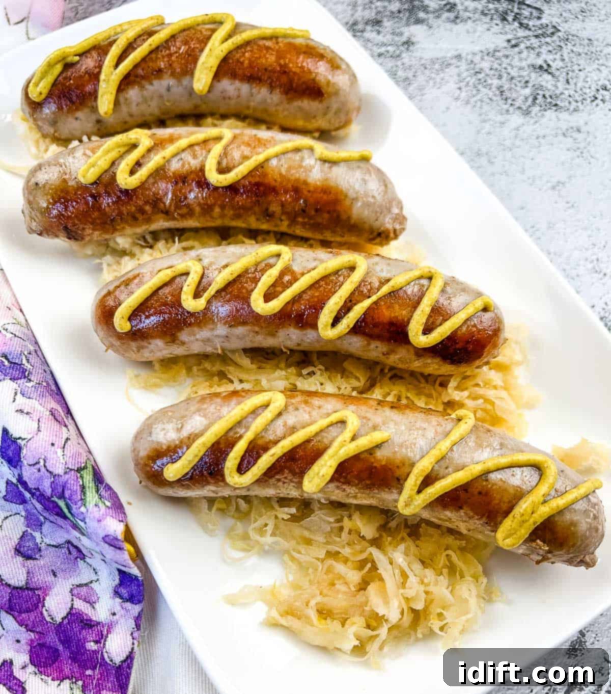 Perfectly cooked sausage with mustard on top of sauerkraut on a white platter, ready to be served from a Blackstone griddle