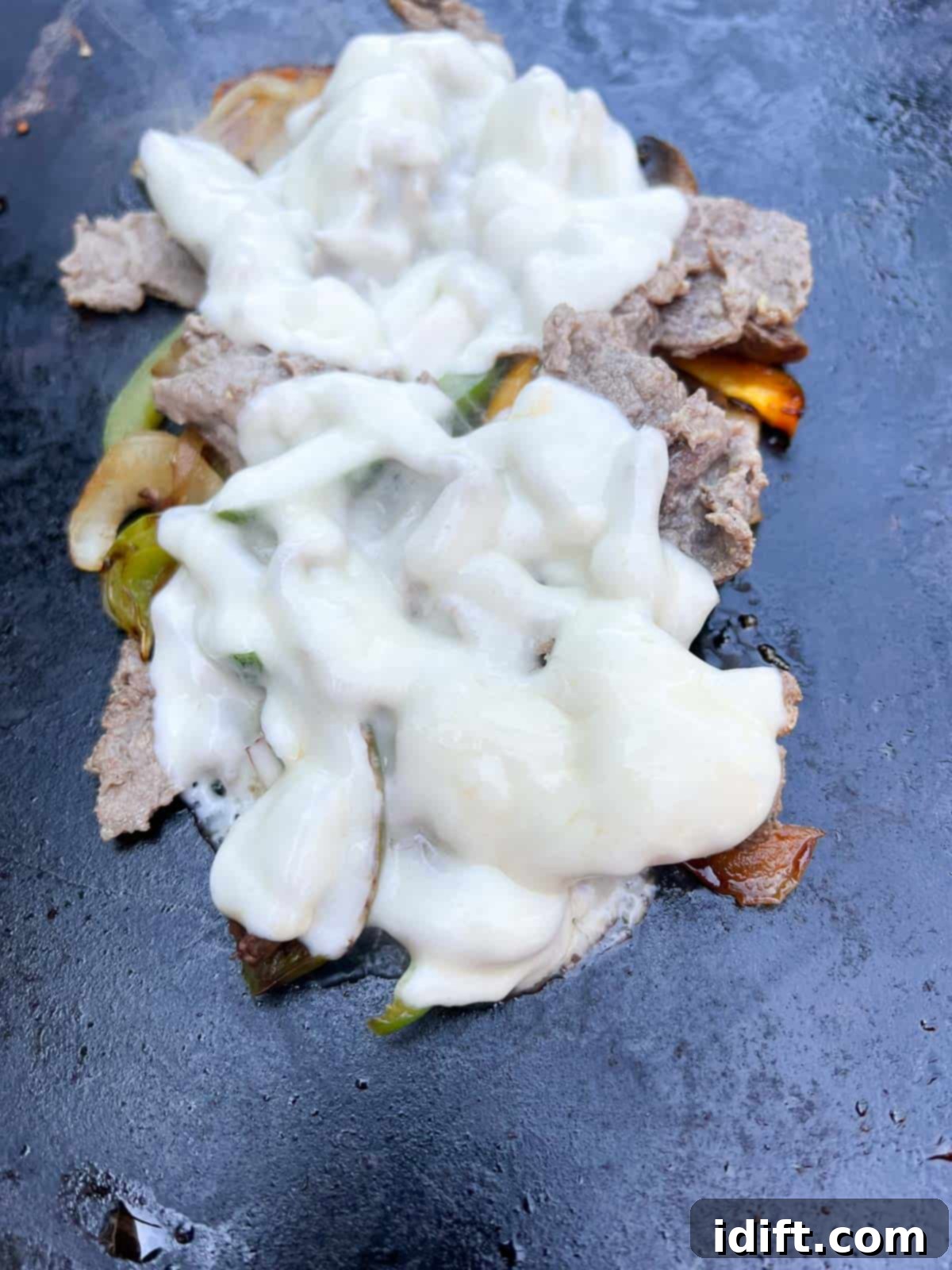 Cooked meat and vegetables topped with Provolone cheese and covered with a cooking dome on the Blackstone griddle to melt.
