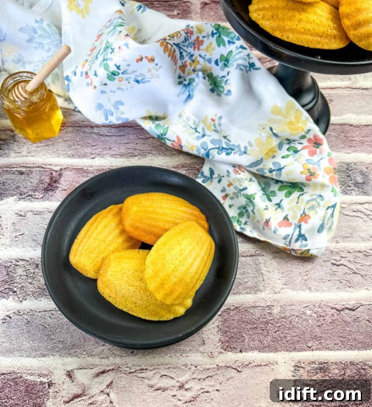 honey butter cornbread madeleines on a black plate with honey in the background